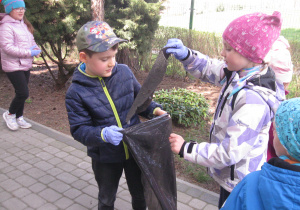 Dzieci zbierają śmieci z ogródka przedszkolnego.