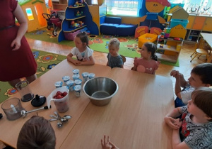 Dzieci siedzą przy stole i będa robić koktajl truskawkowy.