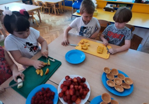 Dzieci kroją nadeskach owoce.