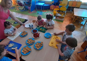 Dzieci przy stole kroją owoce do dekoracji babeczek.