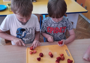 Chłopcy kroją truskawki.