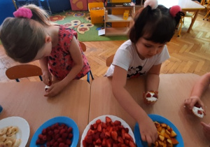 Dzieci dekorują babeczki owocami.