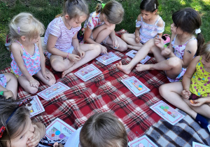 Dzieci siedzą na kocu. Dzieci grają w bingo.
