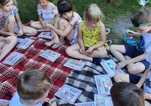 Dzieci siedzą na kocu. Dzieci grają w bingo.