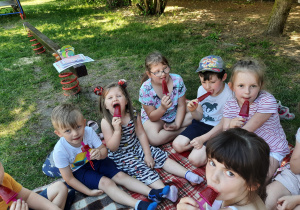 Dzieci siedzą na kocu. Dzieci jedzą lody.