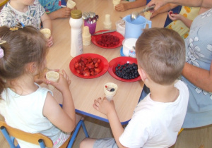 Dzieci dodają owoce do rożków lodowych.
