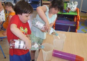 Dzieci nalewają wodę mineralną do dzbanków.