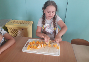 Dziewczynka kroi pomarańczę.