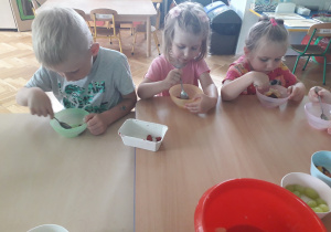 Dzieci jedzą sałatkę owocową.