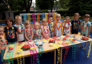 Dzieci stoją przy stole pełnym owoców.
