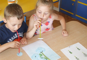 Dzieci przenoszą papierowe kółko dmuchawca za pomocą słomki.