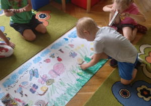 Dzieci maliją łąkę na dużym arkuszu papieru.