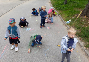 Dzieci malują kredą na asfalcie.