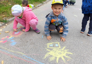 Dzieci malują kredą na asfalcie.
