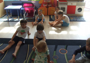 Dzieci siedzą na dywanie i dotykają palcami rąk stóp.