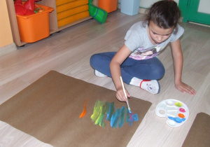Dziewczynka maluje na dużym arkuszu pionowe kreski.