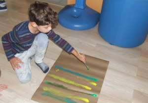 Chłopiec maluje na dużym arkuszu pionowe kreski.