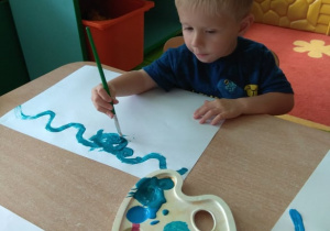 Chłopiec maluje farbami.