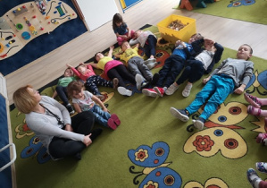 Dzieci leżą na dywanie, na plecach z ętymi oczami i słuchają muzyki