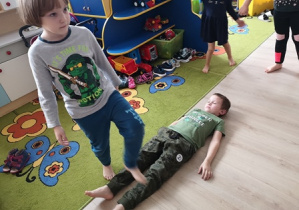 Chłopiec przechodzi nad leżącym kolegą na podłodze