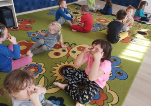 Dzieci siedząc na dyanie dotykaja palcami swoich zamknietych oczu