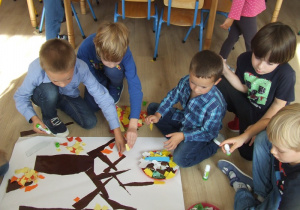 Dzieci przyklejają papiery na duży karton.