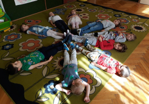 Dzieci leżą na dywanie tworząc gwiazdę.