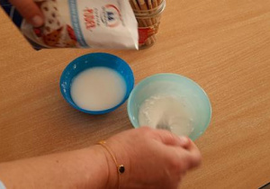 W miseczkach nauczycielka rozpuszcza cukier puder z wodą.