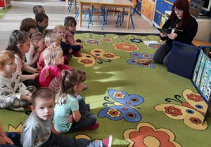 Dzieci siedząc na dywanie słuchają opowiadania.