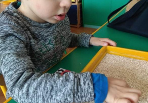 Chłopiec rysuje palcem wzory na tacce z kaszą.