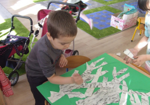 Chłopiec przykleją gałęzie z papieru.