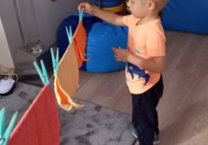 Chłopiec zapina ścieręczkę na sznurku za pomocą klamerek