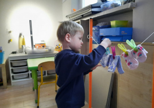 CChłopiec przypina skarpetki na sznurku za pomocą spinaczy do bielizny.
