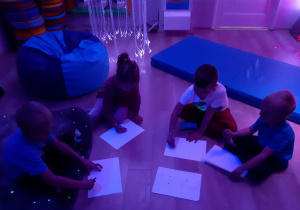 Dzieci siedzą na podłodze w kole i rysują.