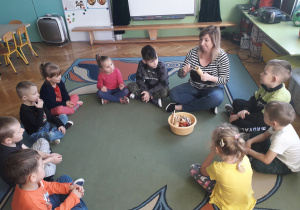 Dzieci siedzą razem z Panią nauczycielką w kole i grają na instrumentach.