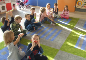 Dzieci siedzą na dywanie i jedzą jabłuszka.