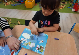 Dziewczynka odrysowuje szablon kropelki na niebieskiej kartce.