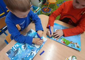Chłopcy odrysowują szablony kropelki i chmury na niebieskiej kartce.