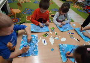 Dzieci odrysowują szablony na niebieskiej kartce.