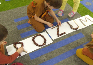 Dzieci układają napis z kasztanów.