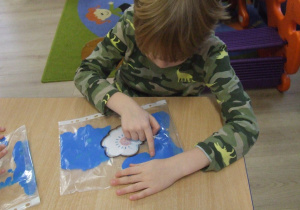 Dzieci rozprowadzają farbę znajdującą się w foliowej koszulce.