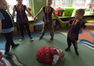 Dzieci tańczą w kole a dziewczynka leży na dywanie.