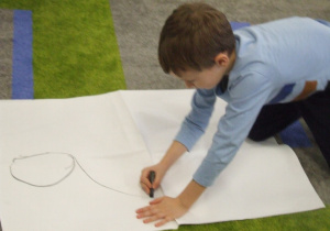 Chłopiec rysuje misia na dużym arkuszu papieru.