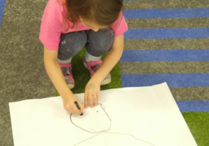 Dziewczynka rysuje misia na dużym arkuszu papieru.