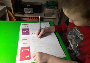 Chłopiec pisze literę po śladzie.