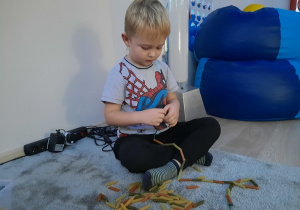 Chłopiec nawleka makaron na sznurówkę.