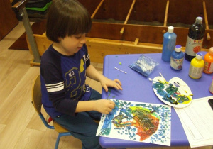 Chłopiec maluje patyczkami higienicznymi.