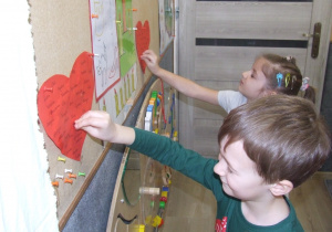 Dzieci wkłuwają pinezkę w serce z imionami.