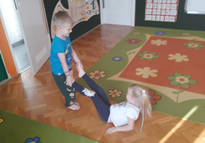 dziecko przytrzymuje dziecko za nogi na wysokości kostek, lekko przeciąga je w różnych kierunkach.