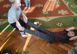 dziecko przytrzymuje dziecko za nogi na wysokości kostek, lekko przeciąga je w różnych kierunkach.